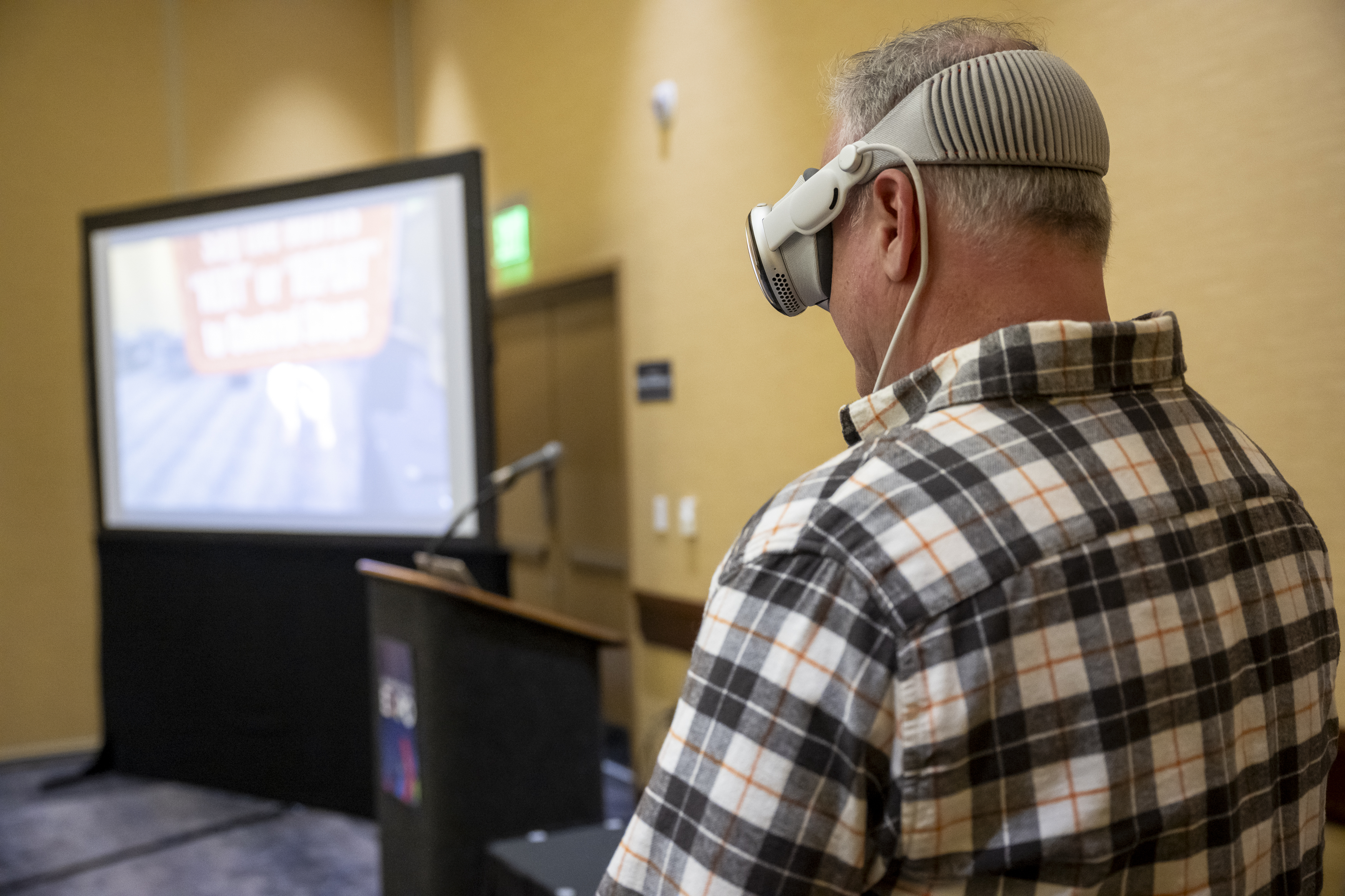 Participant wearing a VR headset, focused on a screen displaying interactive content in a conference setting.
