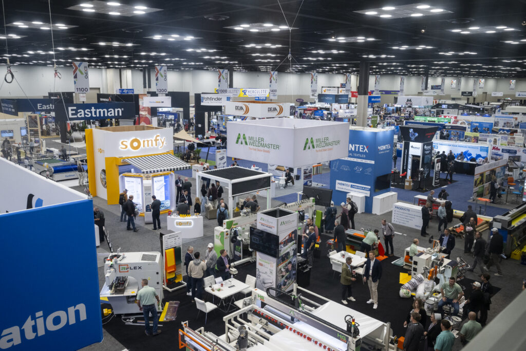 Aerial view of a bustling expo hall with colorful booths, showcasing various companies and people engaging in conversations.