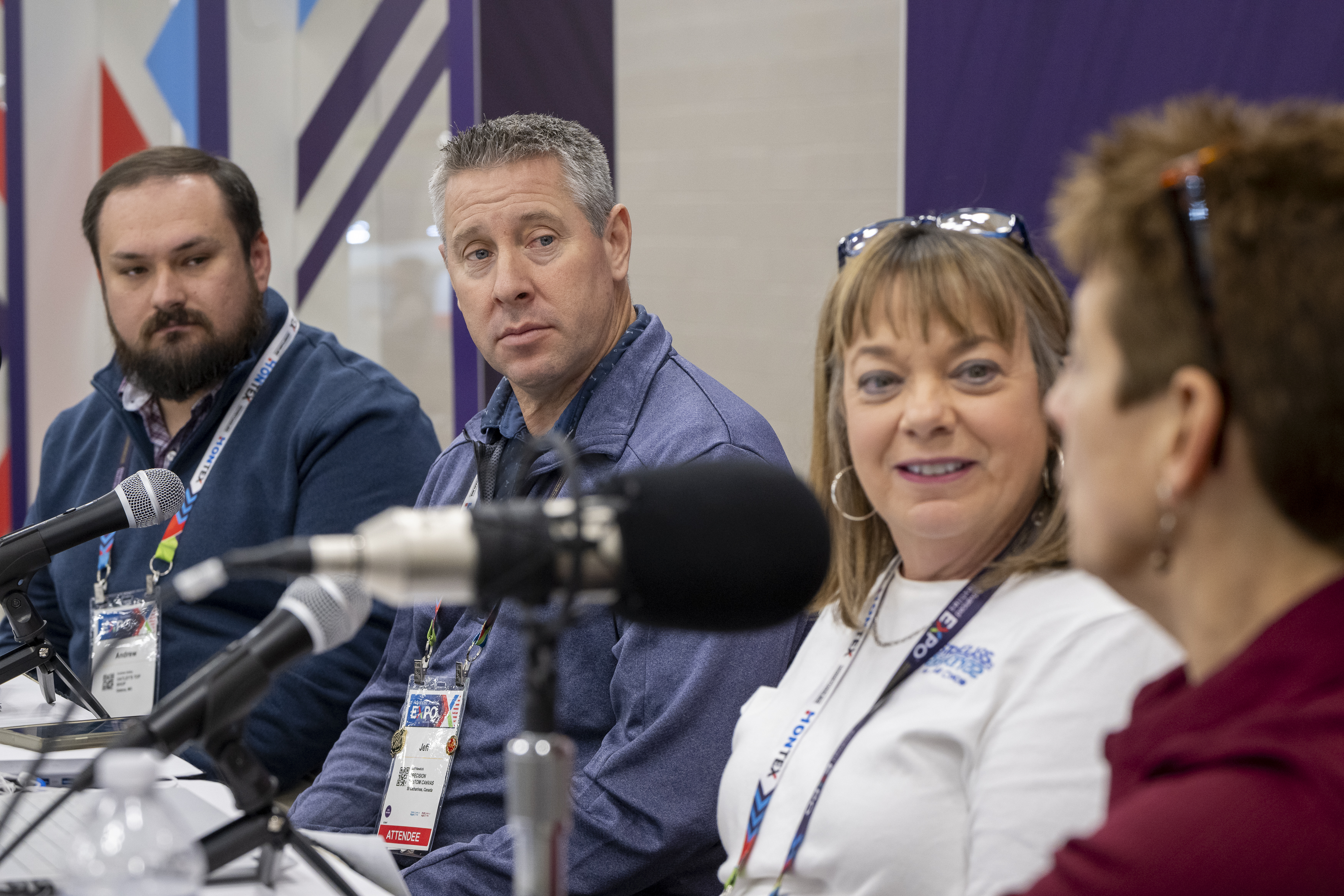 Panel discussion featuring four speakers, with microphones and name tags visible, set against a colorful backdrop.