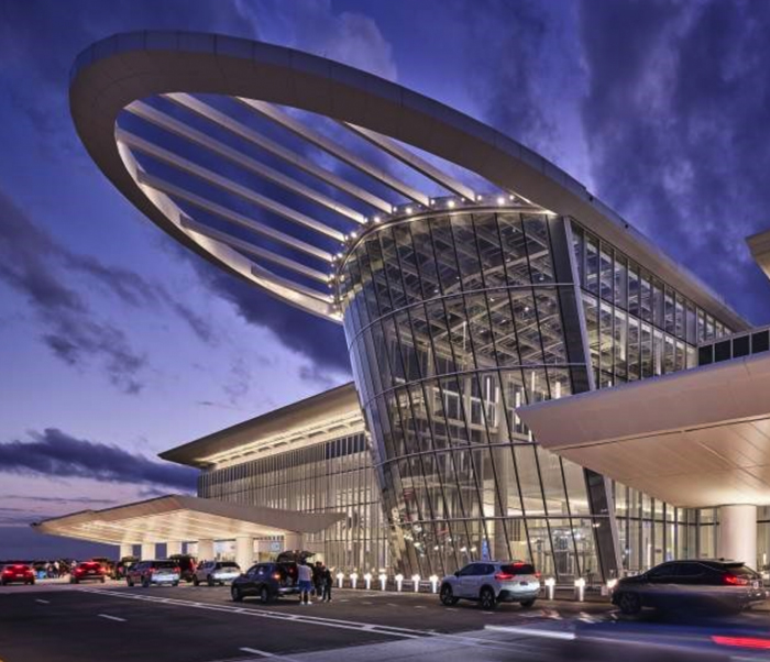 Modern airport terminal with a sleek glass façade, dynamic roof structure, and illuminated entryway, set against a twilight sky.