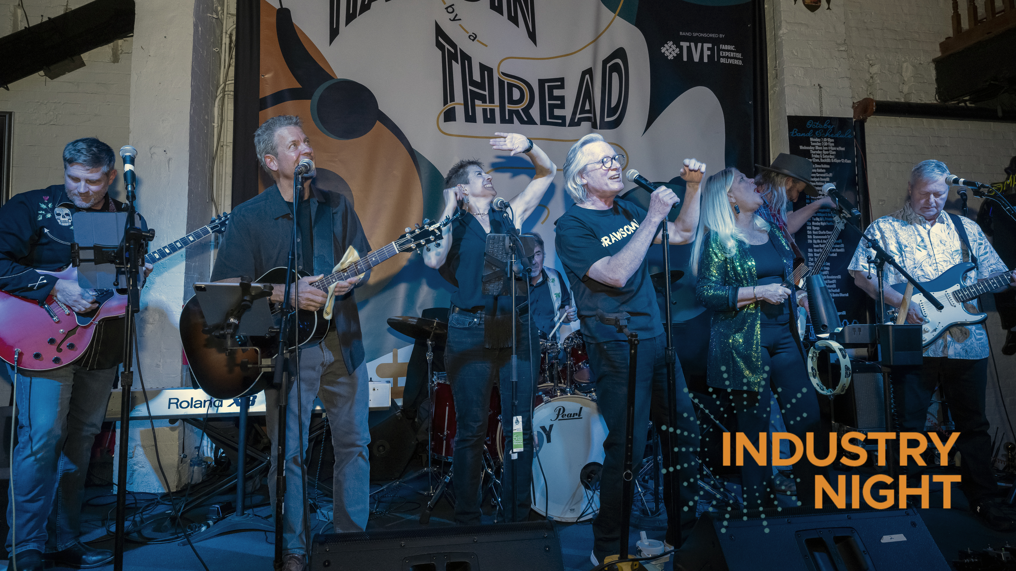 A lively band performance with five musicians on stage, colorful instruments, and a vibrant "Industry Night" banner in the background.