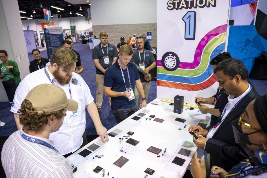 Participants engage at a demo station, examining various materials laid out on a table, with colorful banners in the background.