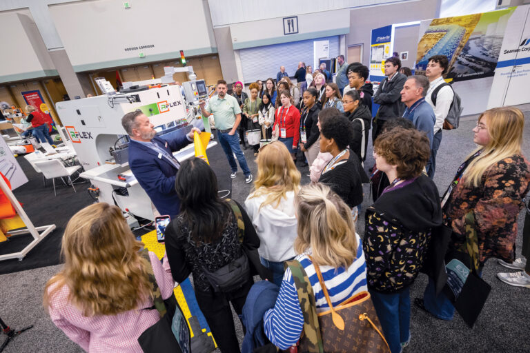 A group of students attentively watches a speaker demonstrate fabric processing techniques at the Advanced Textiles Expo 2025.