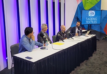 Four panelists discuss textiles at a table, with microphones in front of them, against a colorful backdrop featuring "Talking Textiles."