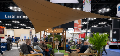 A black retractable awning is showcased in a trade show setting, with attendees engaging nearby and a light-colored backdrop.