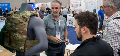 A black retractable awning is showcased in a trade show setting, with attendees engaging nearby and a light-colored backdrop.