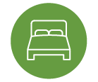 White bed icon on a green circular background, featuring a simple design with two pillows on the mattress.