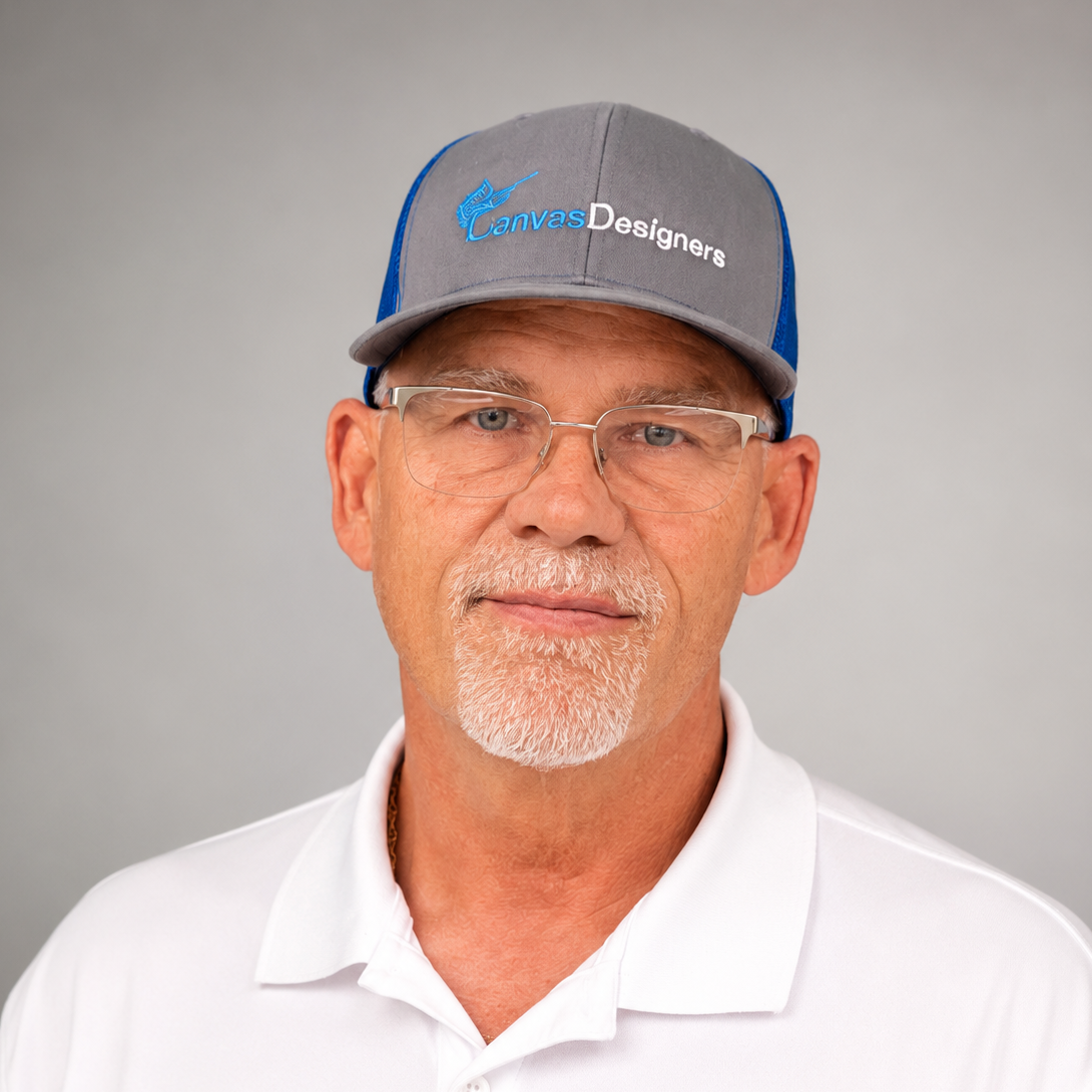 A middle-aged man with glasses and a gray and blue baseball cap, wearing a white polo shirt, faces the camera against a gray background.