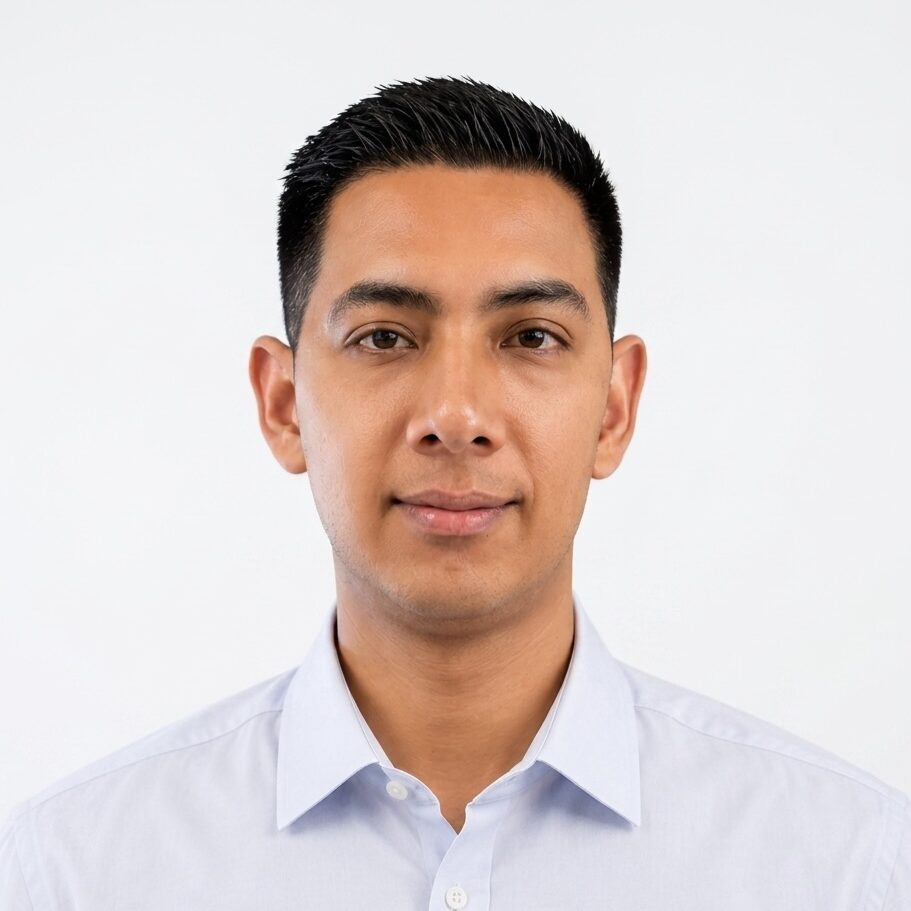 Portrait of a young man with short black hair, wearing a light blue shirt, set against a plain white background.