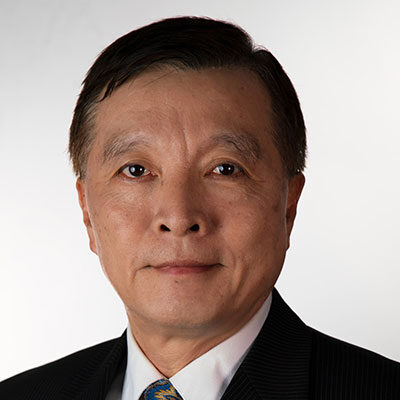 Headshot of a middle-aged man with short dark hair, wearing a black suit and a patterned tie, set against a white background.