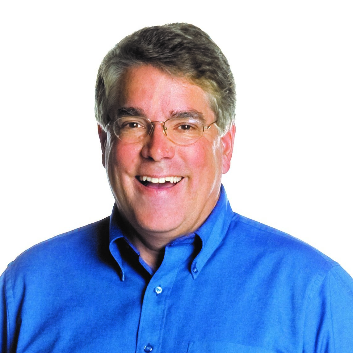 Smiling man wearing glasses and a blue shirt, set against a plain white background. Bright and friendly demeanor.